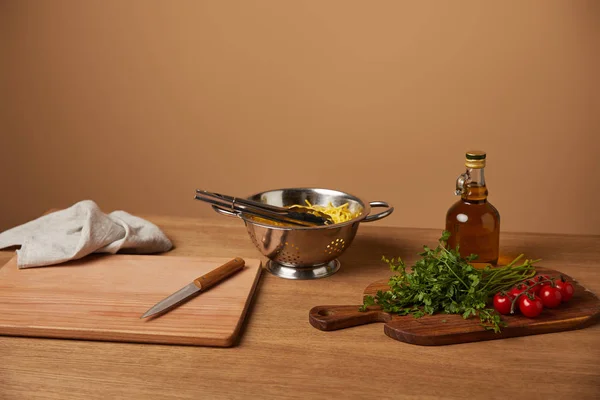 Spaghetti in metal colander with vegetables and olive oil on wooden table — Stock Photo