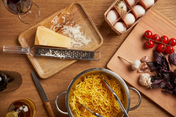 Vue du dessus des spaghettis en passoire métallique entourée de divers ingrédients pour pâtes sur table en bois — Photo de stock