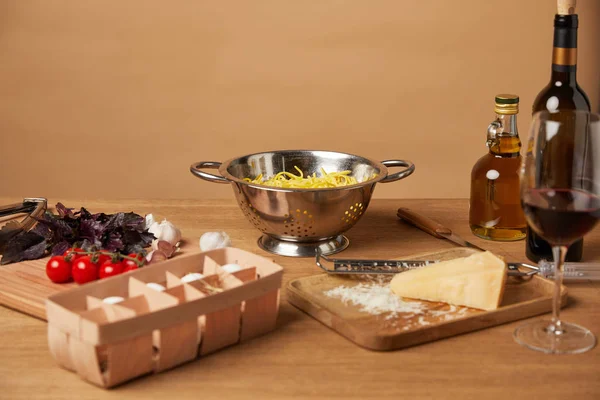 Espaguete em escorredor de metal cercado com ingredientes para massas e vinho em mesa de madeira — Fotografia de Stock