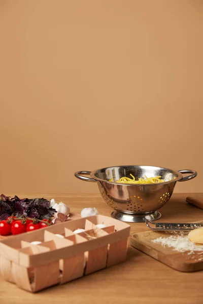 Spaghetti im Metallsieb, umgeben von Zutaten für Pasta auf Holztisch — Stockfoto