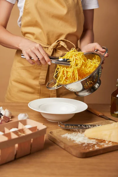 Tiro recortado de mujer poniendo espaguetis en un tazón con pinzas de colador - foto de stock