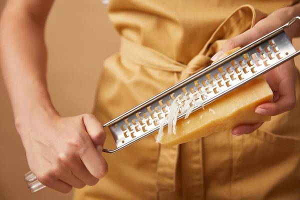 Cropped shot of woman in yellop apron grating cheese — Stock Photo