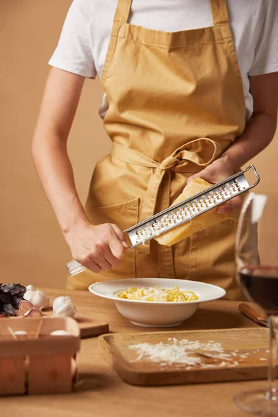 Cropped shot of woman grating cheese while cooking pasta — Stock Photo