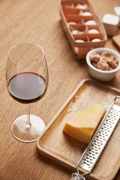 Nahaufnahme von geriebenem Käse und einem Glas Rotwein auf einem Holztisch — Stockfoto