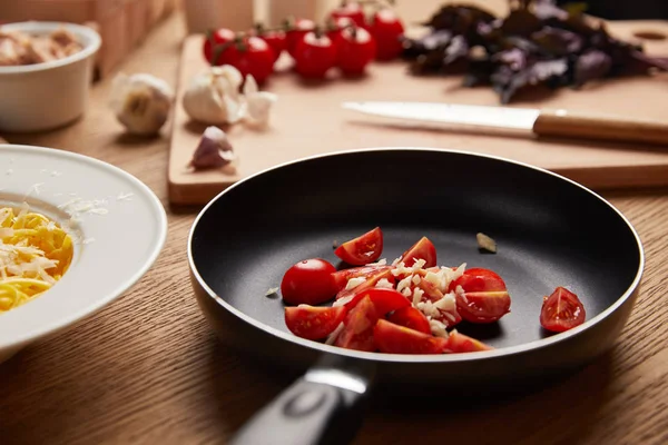 Primer plano de tomates en rodajas y ajo en sartén para pasta sobre mesa de madera — Stock Photo