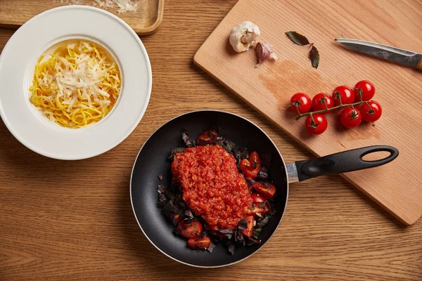 Top view of plate of spaghetti and tomato sauce in frying pan on wooden table — Stock Photo