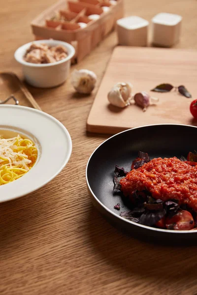 Primer plano de plato de espaguetis y salsa de tomate en sartén sobre mesa de madera - foto de stock