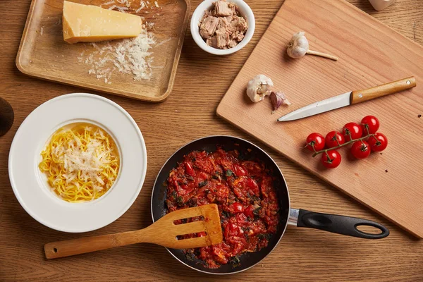 Верхний вид сковородки с томатным соусом для макарон, окруженный ингредиентами на деревянном столе — стоковое фото