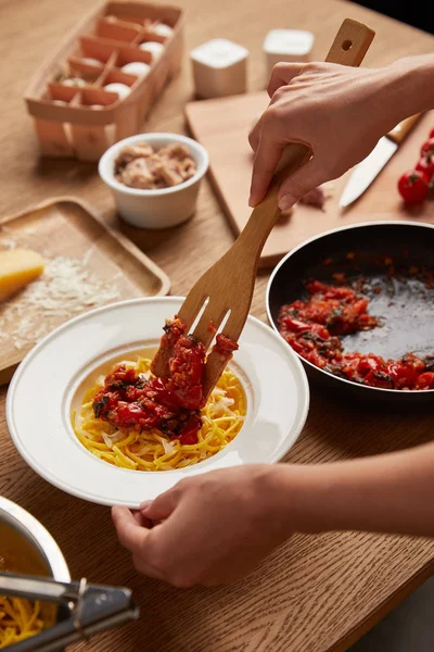 Colpo ritagliato di donna che mette la salsa dalla padella agli spaghetti in piatto — Foto stock