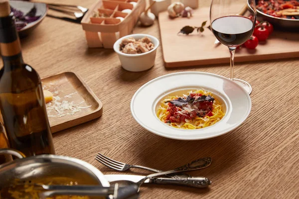 Plate of delicious pasta with ingredients and wine around on wooden table — Stock Photo