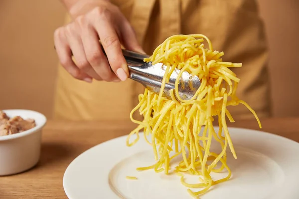 Tiro recortado de la mujer poniendo espaguetis en el plato con pinzas - foto de stock