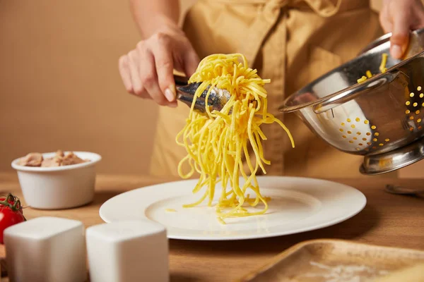 Cropped shot of woman putting spaghetti on plate from colander — Stock Photo
