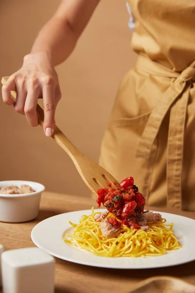 Cropped shot of woman putting sauce onto pasta with wooden spatula — Stock Photo