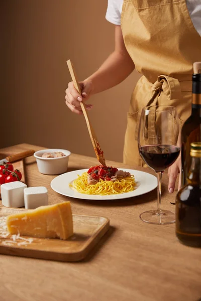 Plan recadré de la femme dans le tablier mettre de la sauce sur les pâtes avec spatule en bois — Photo de stock