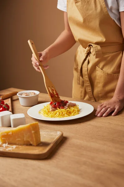 Cropped shot of woman in apron putting pasta in plate on wooden table — Stock Photo