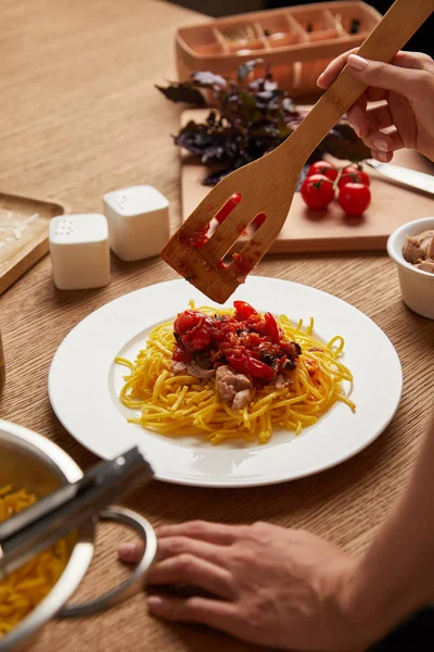 Colpo ritagliato di donna mettendo la pasta in piatto sul tavolo di legno — Foto stock
