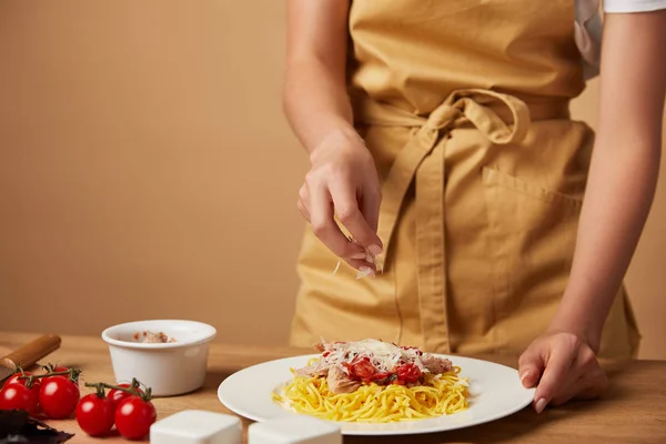 Tiro recortado de la mujer derramando queso rallado en la pasta en el plato - foto de stock