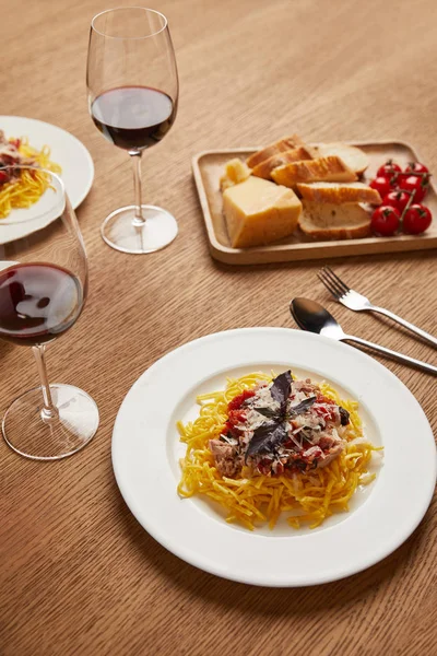 Close-up shot of plates of spaghetti with red wine in glasses on wooden table — Stock Photo