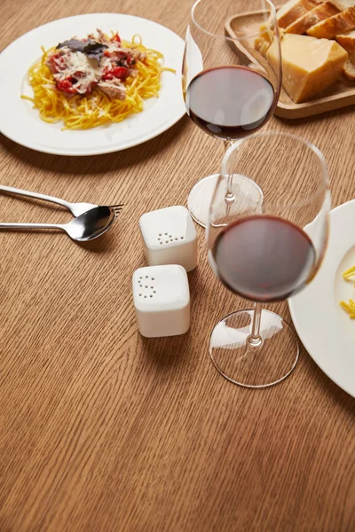 Close-up shot of plates of tasty pasta with red wine in glasses on wooden table — Stock Photo