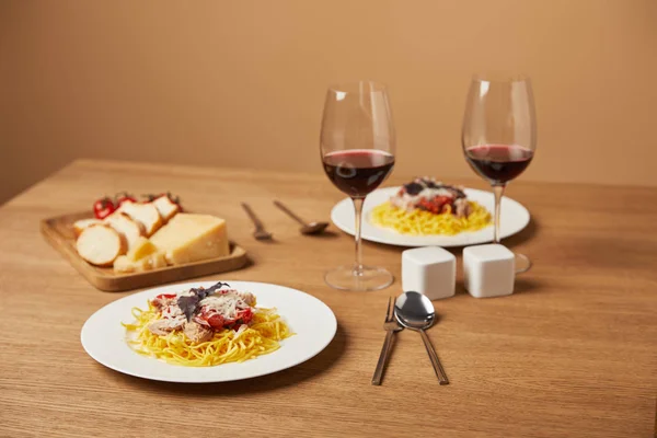 Assiettes de pâtes savoureuses avec du vin rouge dans des verres sur une table en bois — Photo de stock