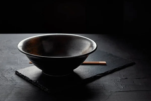 Vue rapprochée du bol vide et des baguettes sur la planche d'ardoise noire — Photo de stock