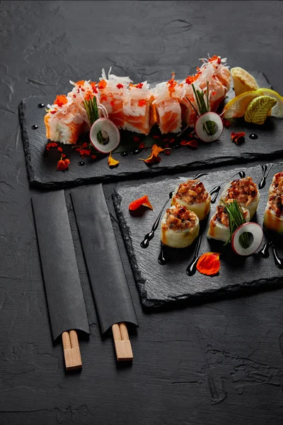 Deliciosos rolos de sushi frescos em tábuas de ardósia e pauzinhos — Fotografia de Stock