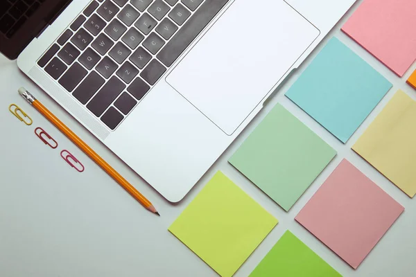 Flat lay of laptop, set of colored paper stickers, pencil and paper clips on white tabletop — Stock Photo