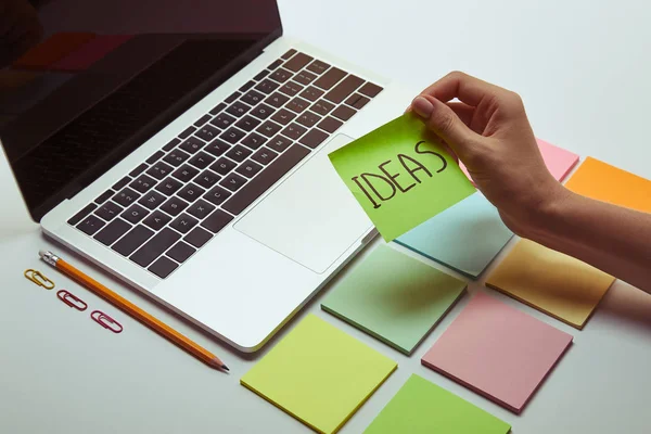 Imagem cortada de mulher segurando papel adesivo com ideias de palavras perto de laptop — Fotografia de Stock