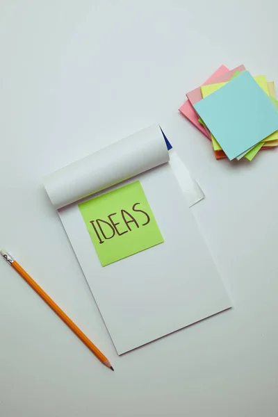 Top view of paper sticker with word ideas in notebook, pencil and pile of note papers on white tabletop — Stock Photo