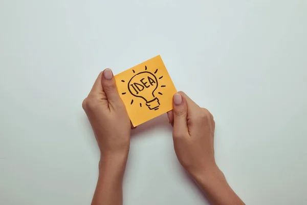 Imagen recortada de mujer sosteniendo pegatina de papel con idea de palabra en bombilla - foto de stock