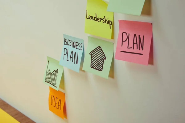 Pegatinas de papel con palabras plan de negocios, liderazgo e idea en la pared - foto de stock