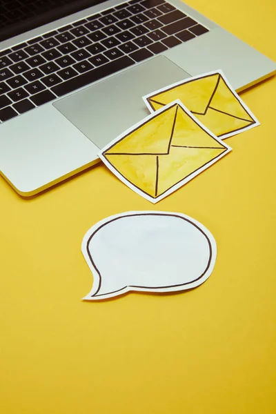 Message signs, speech bubble and laptop on yellow surface — Stock Photo