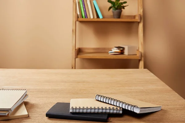 Cadernos em mesa de madeira, prateleiras com livros e plantas em casa — Fotografia de Stock