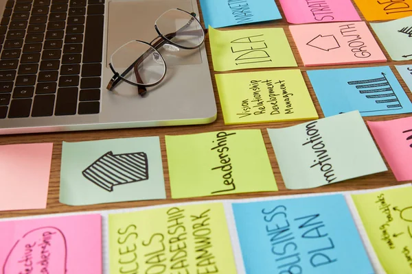 Paper stickers with business strategy and laptop with glasses on tabletop — Stock Photo