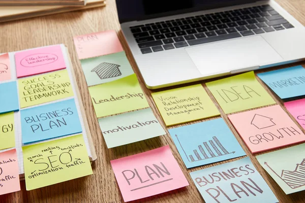 Autocollants en papier coloré avec stratégie d'entreprise et ordinateur portable sur table — Photo de stock