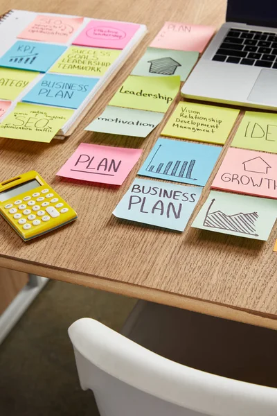 Adesivos de papel com estratégia de negócios, calculadora e laptop na mesa — Fotografia de Stock