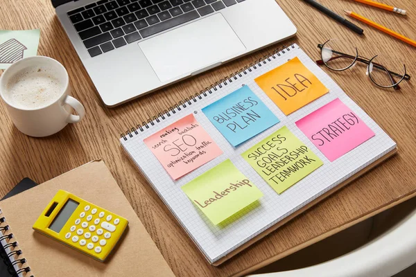 Pegatinas de papel con estrategia de negocio, calculadora, taza de café y portátil en la mesa - foto de stock