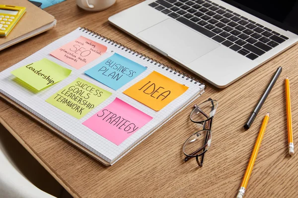 Papieraufkleber mit Geschäftsstrategie auf Notizbuch und Laptop auf Tischplatte — Stockfoto