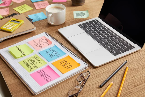 Adesivos de papel com estratégia de negócios, óculos e laptop na mesa — Fotografia de Stock