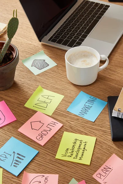 Autocollants en papier avec stratégie d'affaires, tasse de café savoureux et ordinateur portable sur la table — Photo de stock