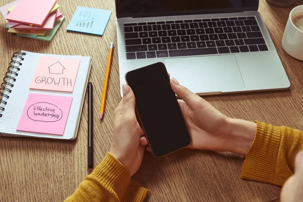 Cropped image of woman holding smartphone with blank screen at table in room — Stock Photo