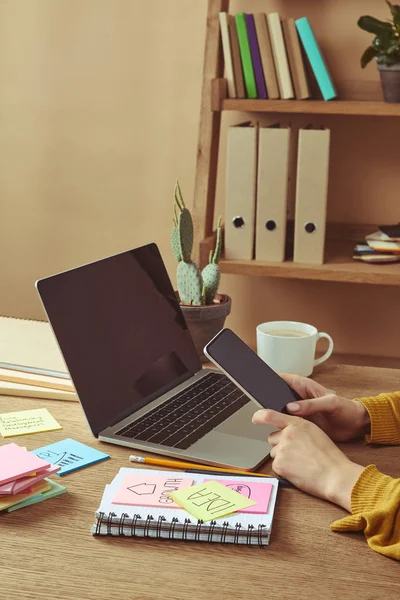 Cropped image of woman holding smartphone with blank screen at table with note paper sheets — Stock Photo