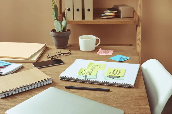 Adesivi di carta con strategia aziendale, laptop e tazza di caffè sul tavolo a casa — Foto stock