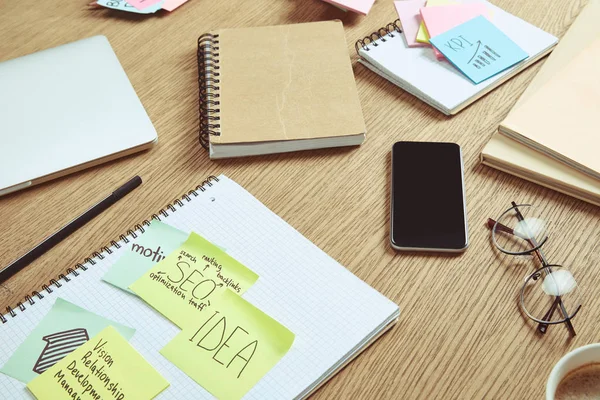 Note paper con strategia aziendale e smartphone con schermo bianco sul tavolo a casa — Foto stock