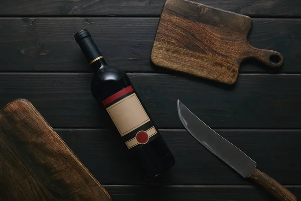 Vista superior de la botella de vino con etiqueta en blanco, cuchillo y tablas de cortar de madera - foto de stock