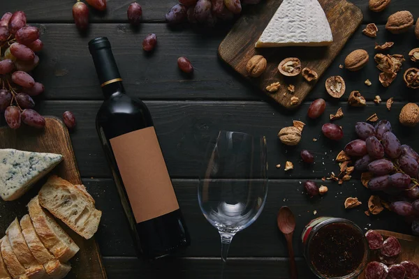 Вид зверху пляшки вина з порожньою етикеткою, склом і різними смачними закусками на дерев'яному столі — стокове фото
