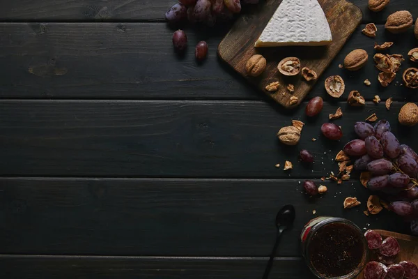 Вид зверху на свіжий стиглий виноград, волоські горіхи, нарізані салямі, варення і смачний сир — стокове фото