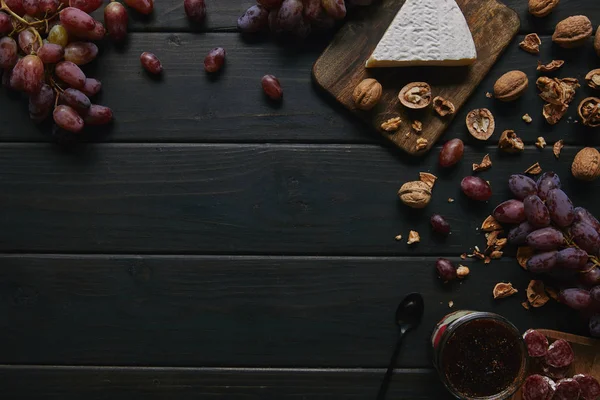 Vista superior de uvas frescas maduras, nueces, salami en rodajas, mermelada y delicioso queso sobre fondo de madera - foto de stock