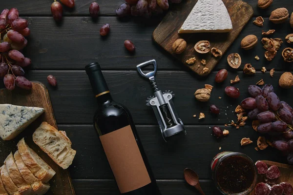 Top view of wine bottle with blank label, corkscrew and various delicious snacks on wooden table — Stock Photo