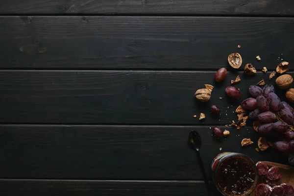 Vista superior de uvas frescas maduras, nueces, salami en rodajas y mermelada sobre fondo de madera - foto de stock